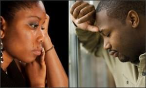 An African American woman with tears on her face and an African American male resting his forehead on his forearm, leaning against a window.