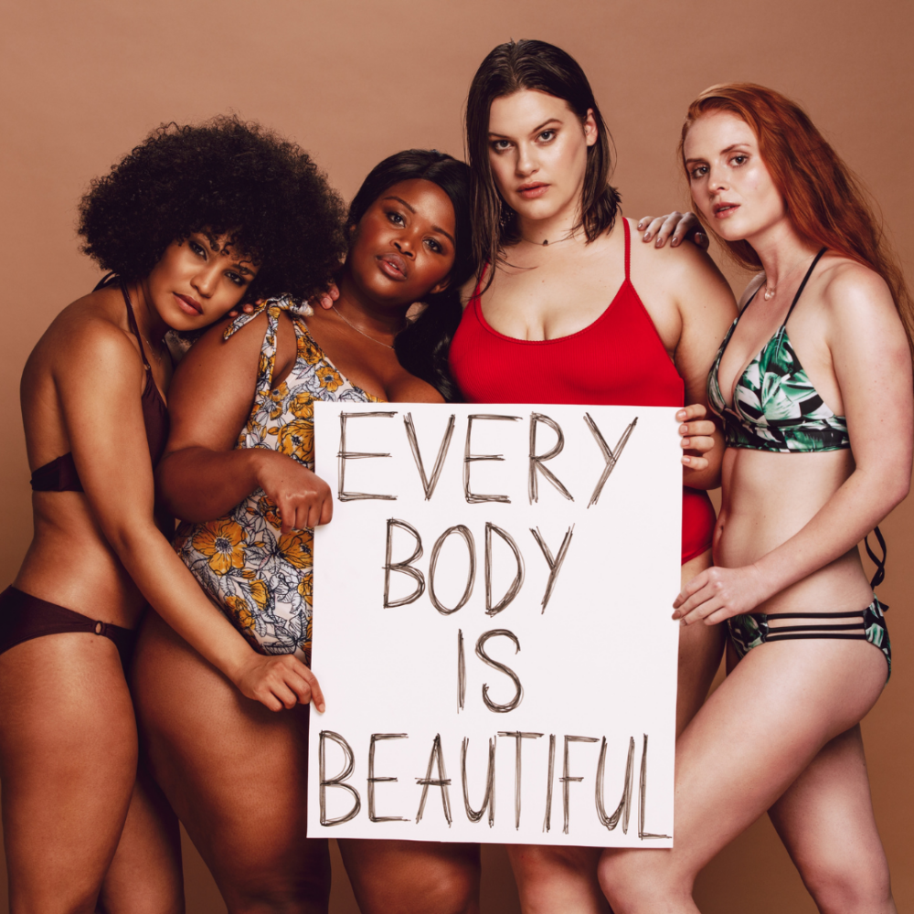 Four females of varying body types and races wearing bathing suits, holding a poster with "Every Body is Beautiful" written on it.