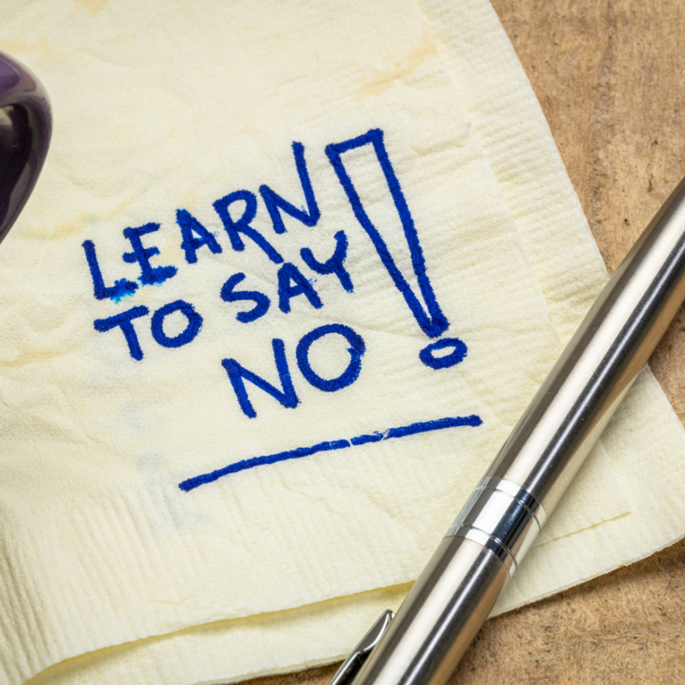A cocktail napkin with "learn to say no" written in blue ink, with a silver pen laying across it.
