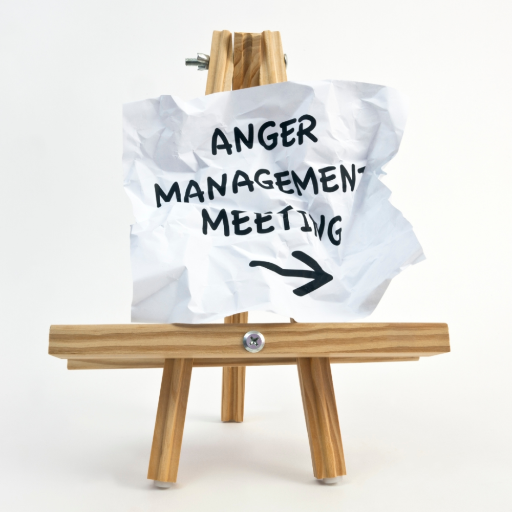 Crumpled paper sitting on a tabletop easel that says Anger Management Meeting with an arrow pointing right.